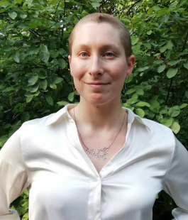 Picture of Terra in front of a green background with a shiny white button down shirt and buzzed haircut