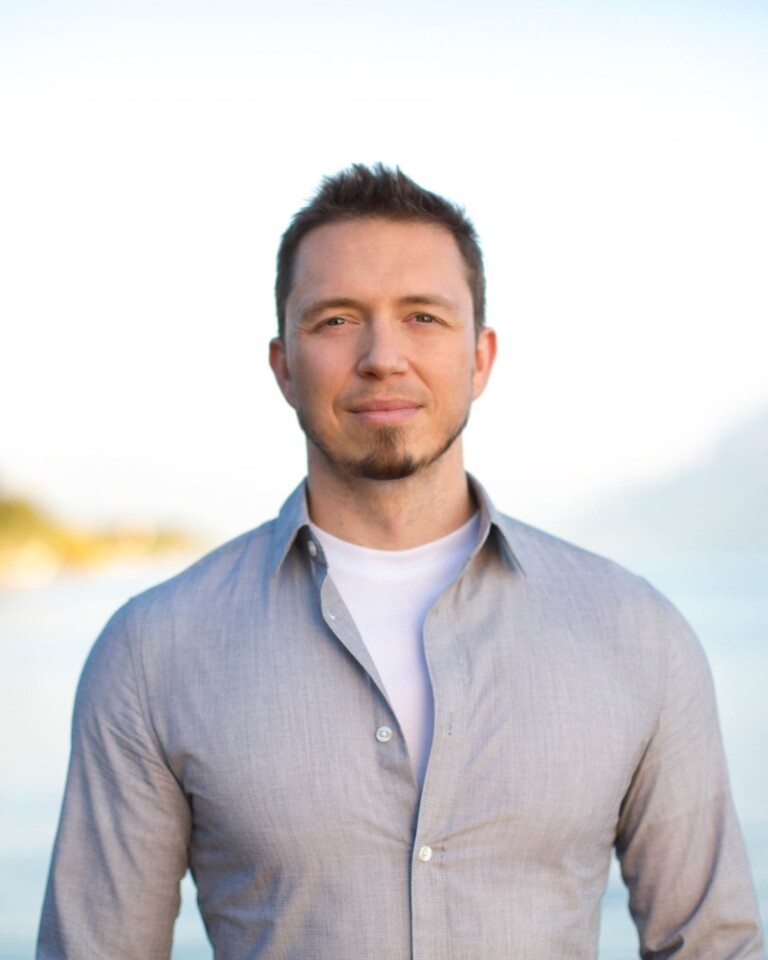 Headshot image of Spencer Watson standing in front of a lake with mountains in the background.