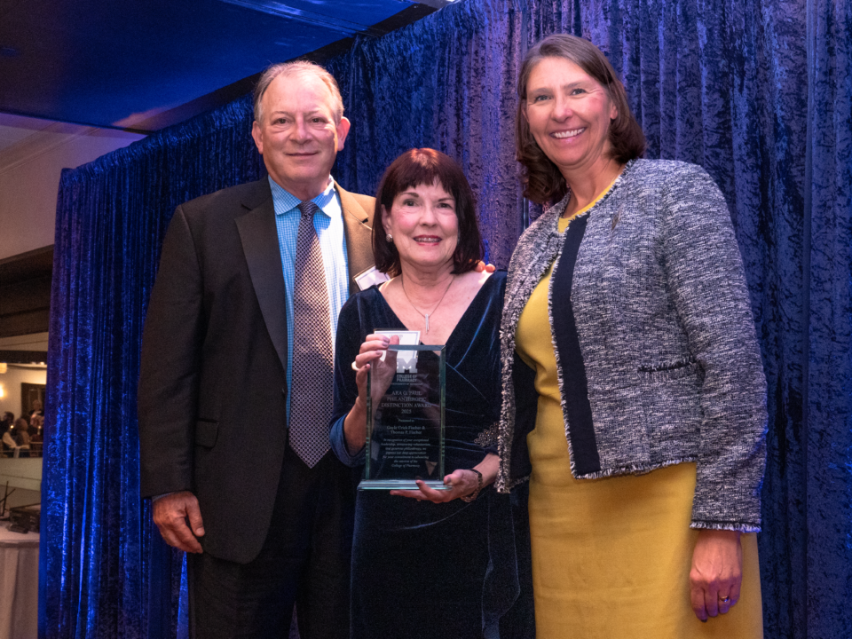 Male and two females smiling at a formal event. The female in the middle is holding an award