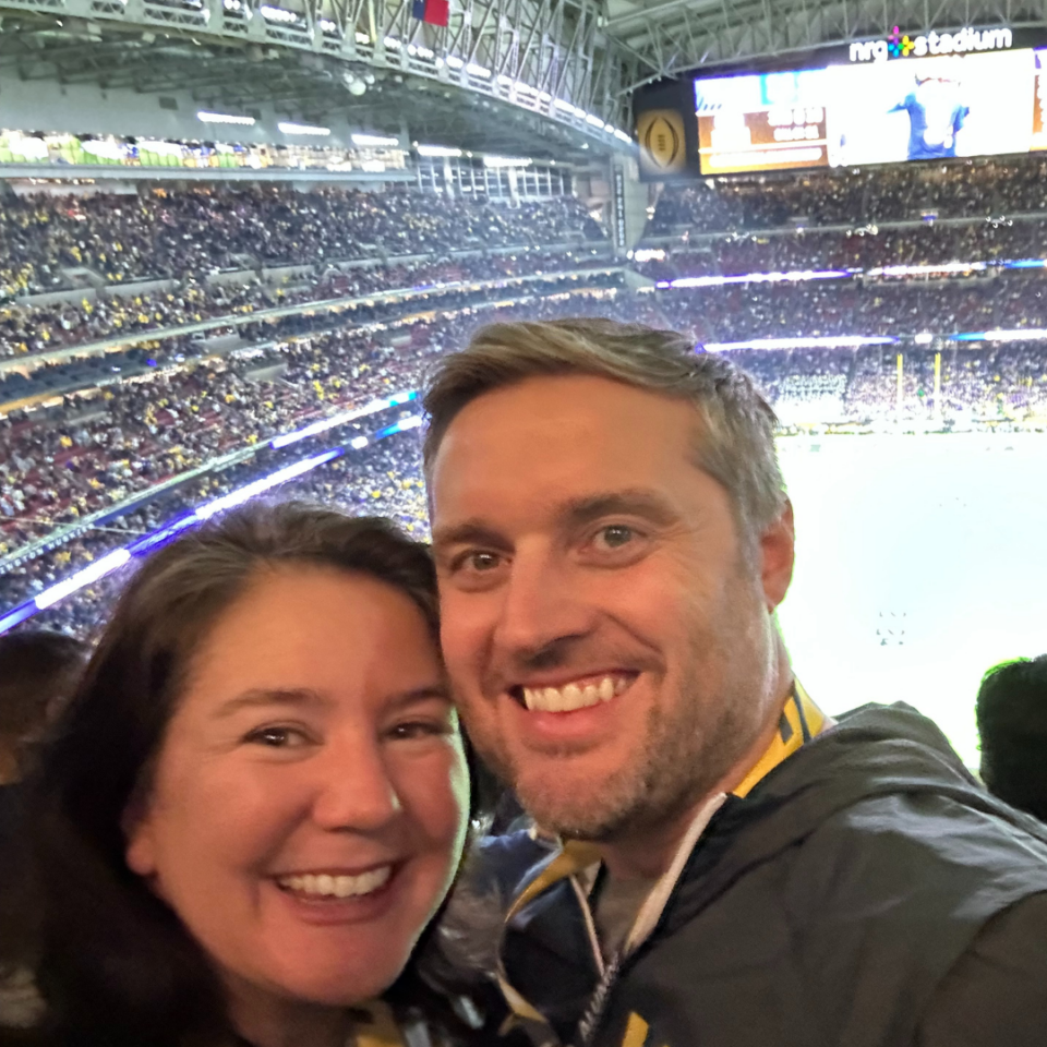 Man and woman pose in front of a sports arena