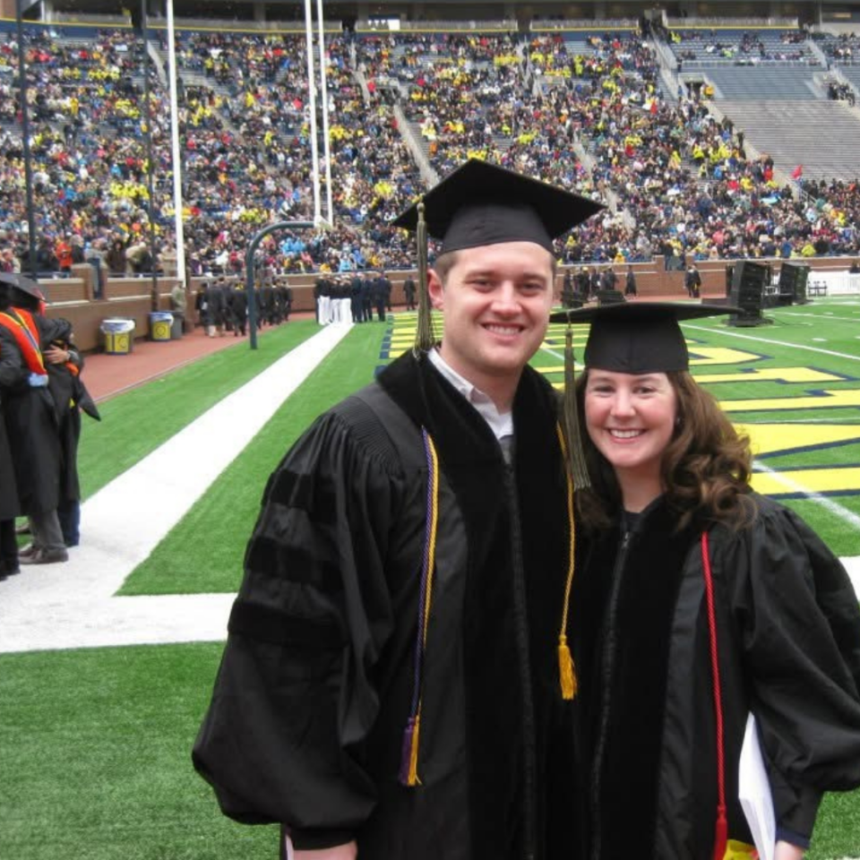 A man and a woman pose together in graduation gowns