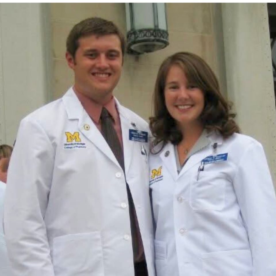 A man and a woman pose together in white coats at a pharmacy white coat ceremony