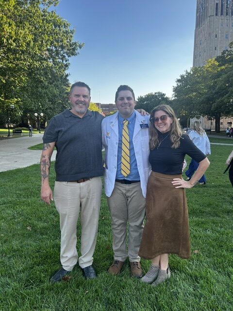 Three adults smiling for a picture outside at the College of Pharmacy White Coat Ceremony