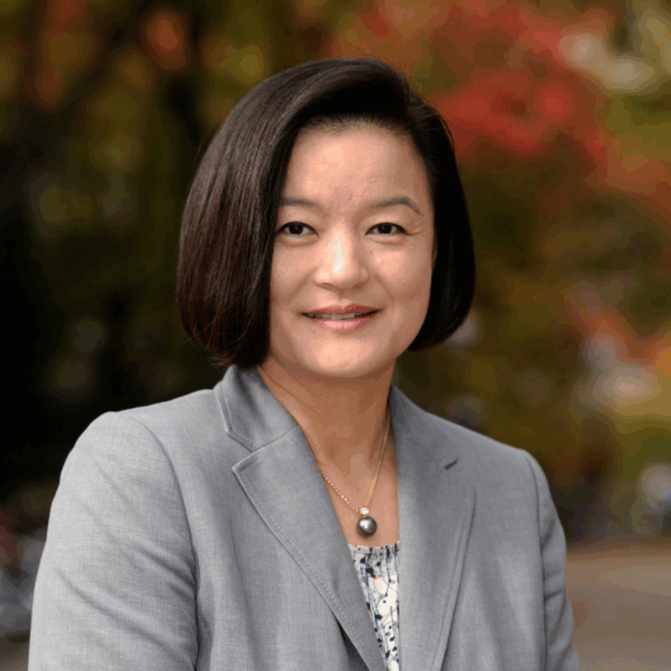 Assistant Dean Hae Mi Choe poses in front of fall trees for a headshot. 